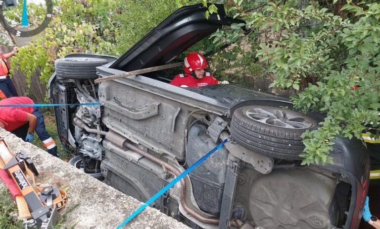 Autoutilitară răsturnată în afara părții carosabile! Două persoane au rămas blocate în interiorul mașinii. Pompierii militari au acționat la foc automat